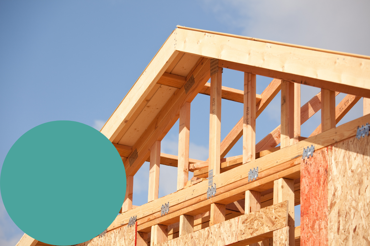 Charpente de maison en bois en construction sur fond de ciel bleu, avec un cercle sarcelle couvrant partiellement le coin inférieur gauche de l'image.